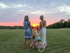 Two women and a child standing in Wild Meadow watching the sunset